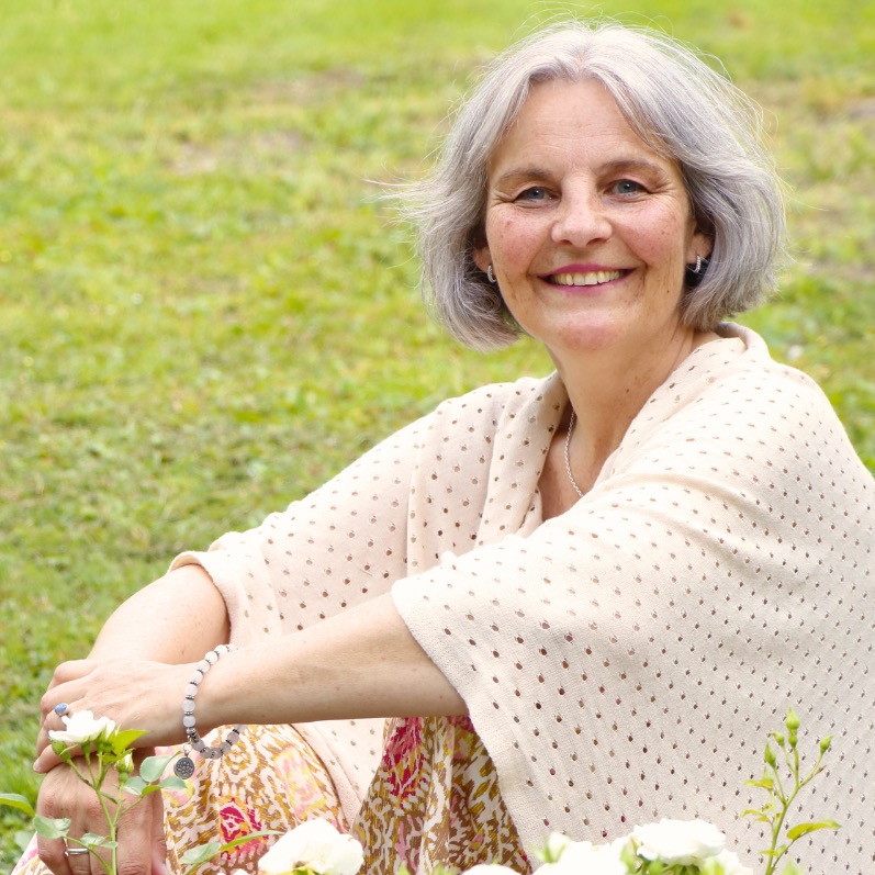 Energetikerin Christine Gningue lächelt herzlich beim Sitzen im Gras hinter weißen Rosen.