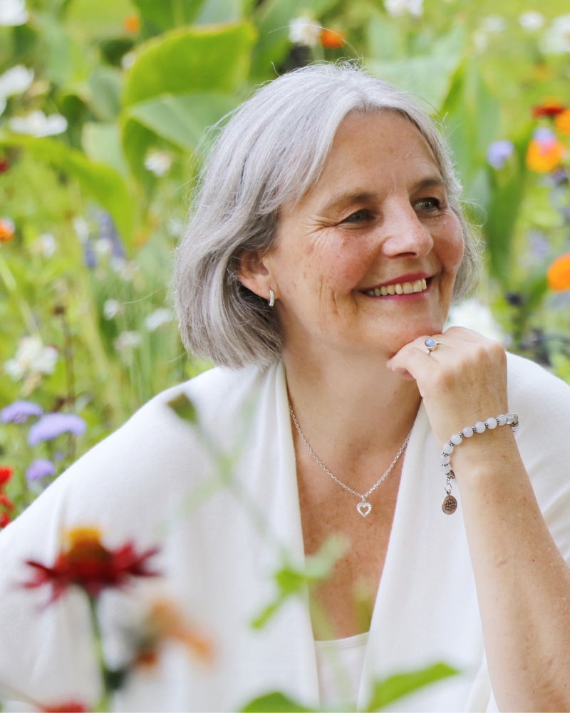 Energetikerin Christine Gningue lächelt entspannt inmitten einer bunten Blumenwiese.