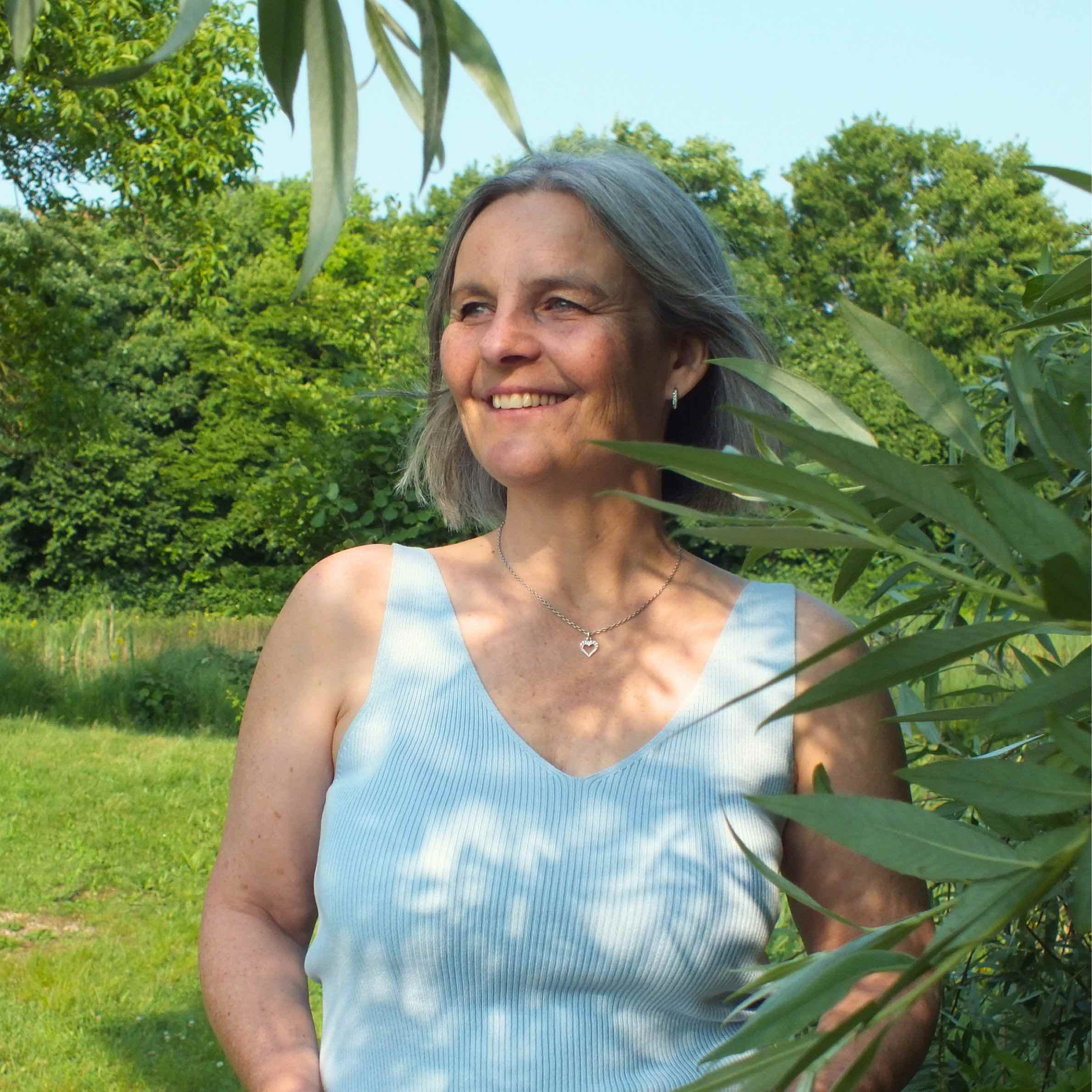 Energetikerin Christine Gningue lächelt und blickt entspannt zur Seite in einer grünen Naturkulisse.