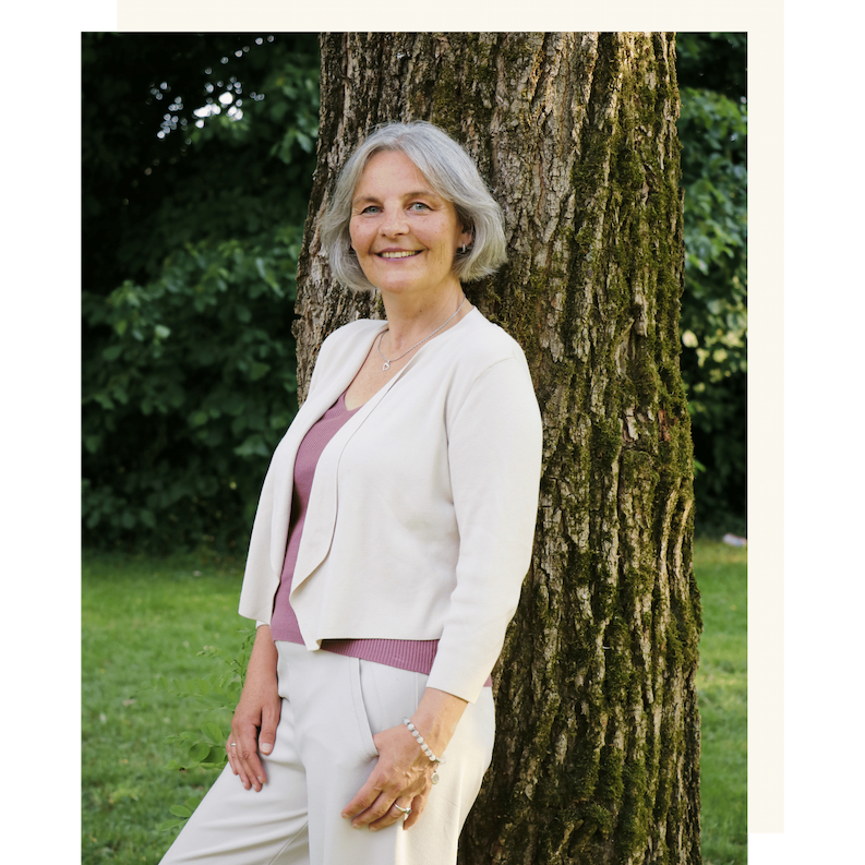 Portrait von Energetikerin Christine Gningue, lächelnd an einen Baum gelehnt im Freien.