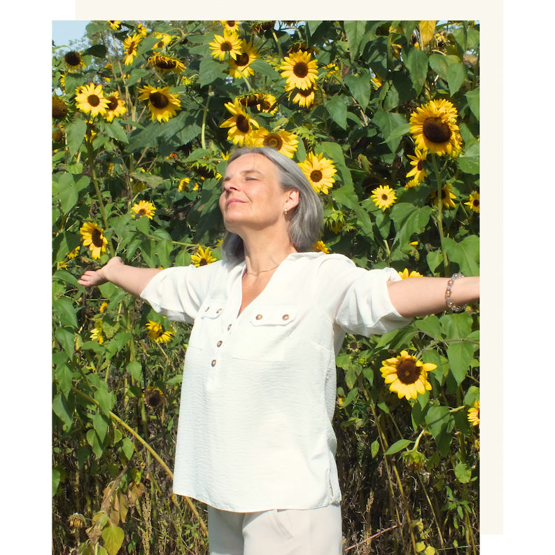Energetikerin Christine Gningue atmet tief ein mit ausgestreckten Armen vor einem Sonnenblumenfeld.