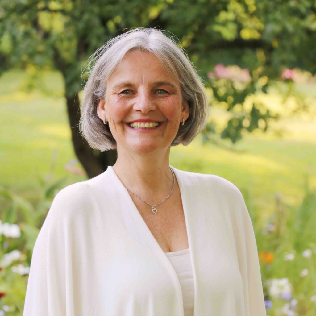 Energetikerin Christine Gningue strahlt herzlich inmitten einer sommerlichen Blumenwiese.