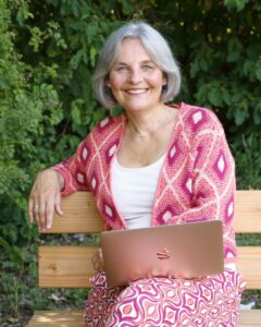 Energetikerin Christine Gningue sitzt mit einem Laptop lächelnd auf einer Holzbank im Grünen.