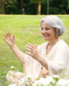 Energetikerin Christine Gningue lächelt entspannt bei einer Energieübung mit erhobenen Händen auf einer Wiese.