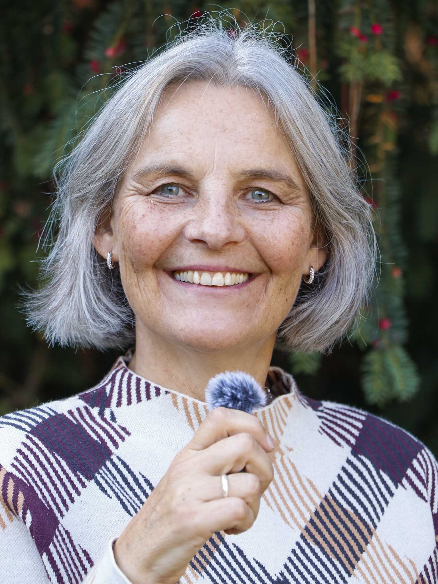 Energetikerin Christine Gningue lächelt herzlich in die Kamera und hält ein Mikrofon für Audioaufnahmen.
